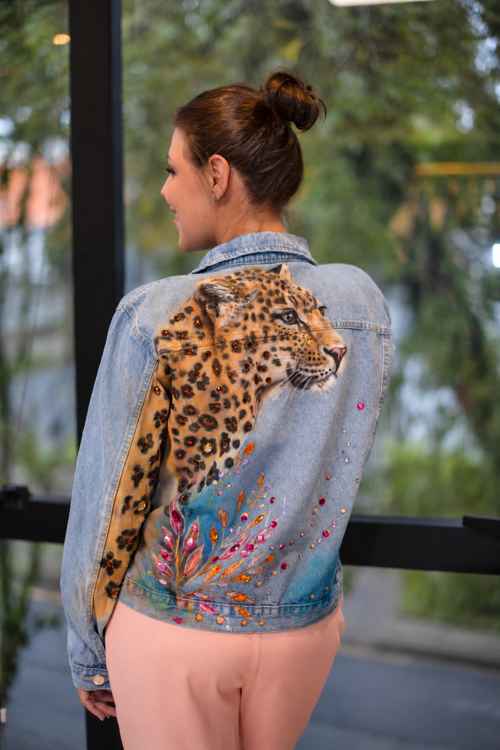 Jaqueta jeans com onça-pintada que desce pela manga, cristais âmbar nas pintas e ramos de pedras rosa e laranja